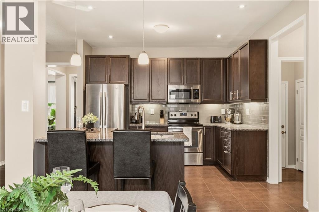 Kitchen featuring dark wood cabinetry, stainless steel appliances, speckled countertops, a tile backsplash, and an island with pendant lighting - 42 Yager Drive, Binbrook, ON - Indoor Photo Showing Kitchen With Stainless Steel Kitchen With Upgraded Kitchen