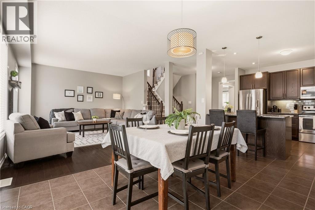 Open-concept living space featuring a dining area with a contemporary chandelier, a kitchen with dark wood-finish cabinetry and stainless steel appliances, and a living room with wood-finish flooring - 42 Yager Drive, Binbrook, ON - Indoor Photo Showing Other Room
