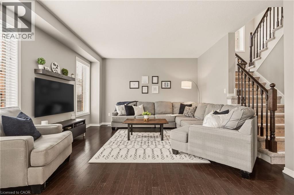 Spacious living area featuring dark wood-finish flooring, a contemporary staircase with dark wood banister and balusters, and multiple windows with blinds - 42 Yager Drive, Binbrook, ON - Indoor Photo Showing Living Room