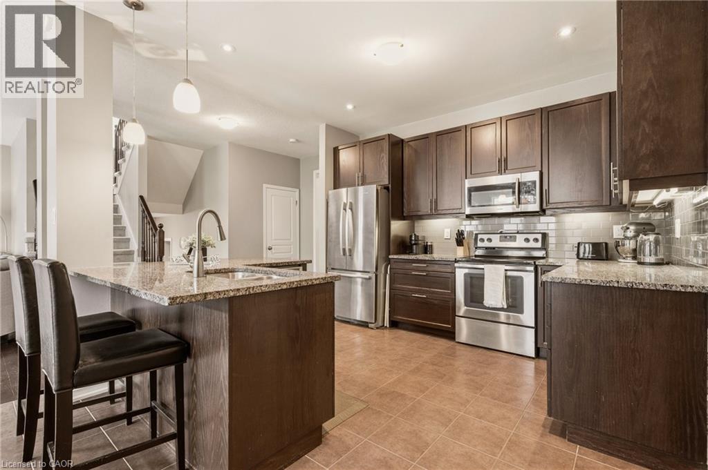 Kitchen featuring dark wood cabinetry, stainless steel appliances, a tile backsplash, and granite countertops - 42 Yager Drive, Binbrook, ON - Indoor Photo Showing Kitchen With Stainless Steel Kitchen With Upgraded Kitchen