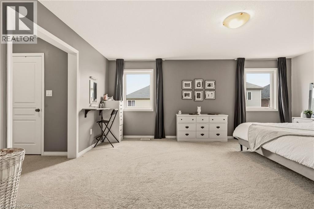 Spacious interior featuring neutral carpeting, two large windows with dark drapery, a flush-mount ceiling light, and a white interior door - 42 Yager Drive, Binbrook, ON - Indoor Photo Showing Bedroom