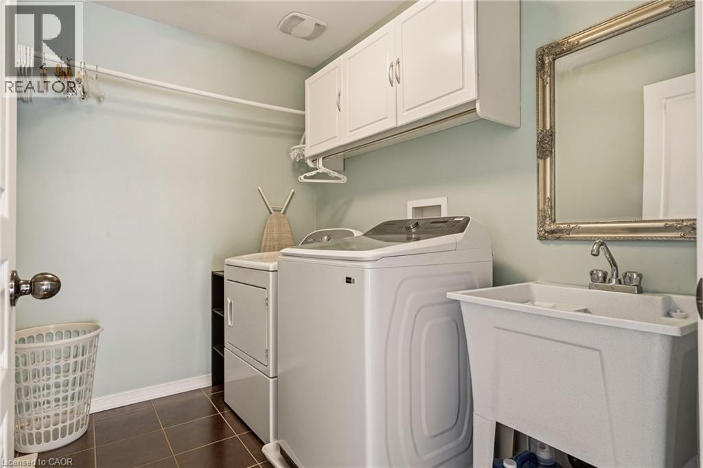Upper-level laundry room featuring dark tile flooring, white shaker-style cabinetry, and a utility sink with a chrome faucet - 42 Yager Drive, Binbrook, ON - Indoor Photo Showing Laundry Room