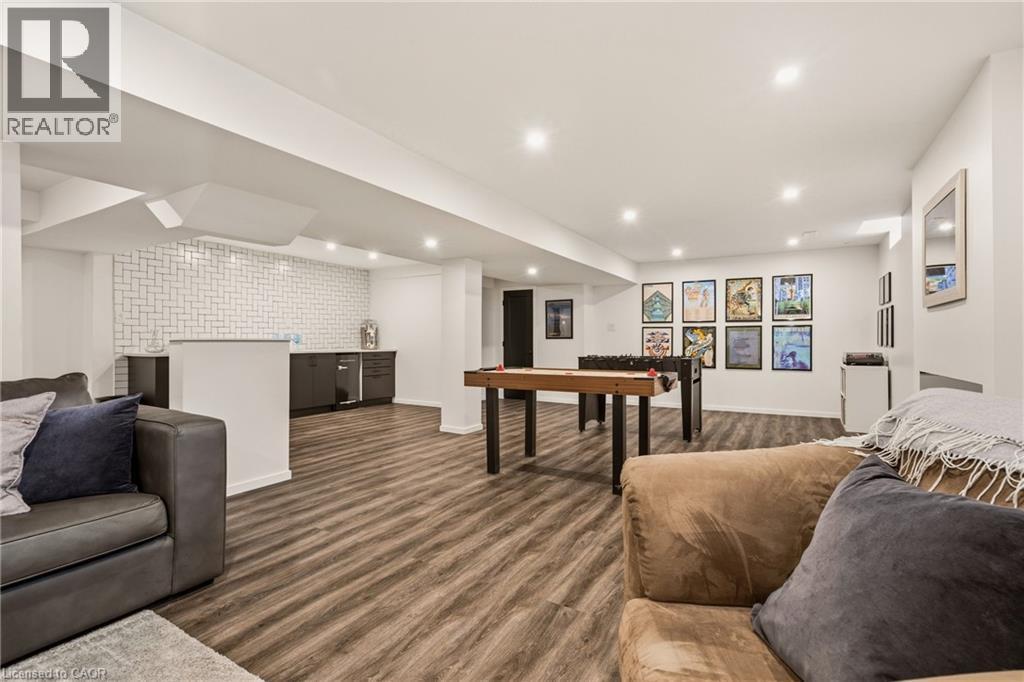 Spacious lower level featuring wood-finish flooring, recessed lighting, and a built-in wet bar with dark cabinetry and a tile backsplash - 42 Yager Drive, Binbrook, ON - Indoor