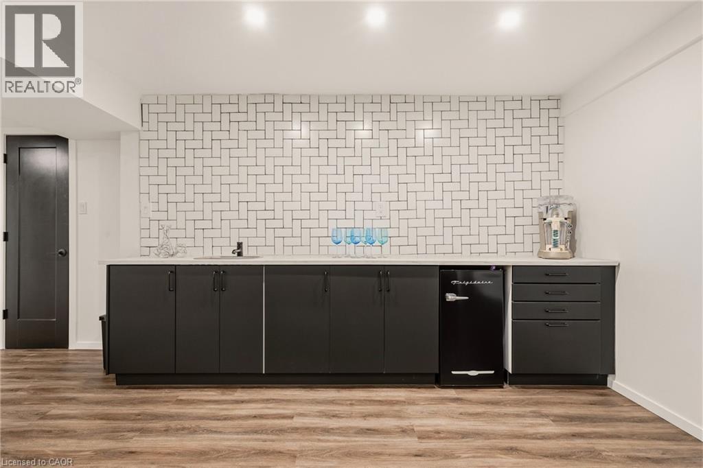 Wet bar featuring a herringbone tile backsplash, integrated sink, and dark cabinetry - 42 Yager Drive, Binbrook, ON - Indoor Photo Showing Other Room