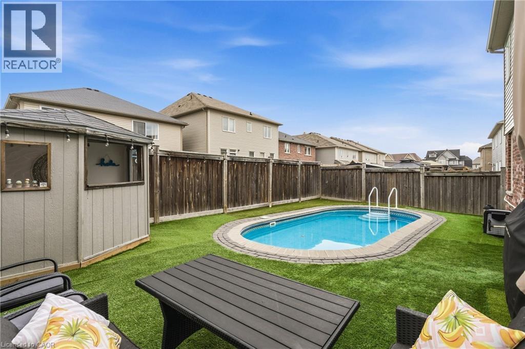 Backyard featuring an oval swimming pool with perimeter paver surround, artificial turf, wood privacy fencing, and a built-in outdoor cabana bar - 42 Yager Drive, Binbrook, ON - Outdoor With Backyard
