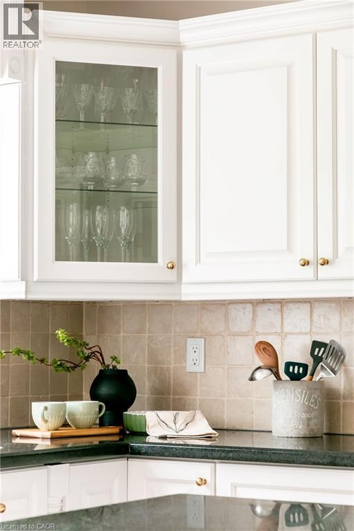 White upper cabinetry with gold-finish hardware, glass-front display cabinet, dark stone countertops, and a light-toned square tile backsplash - 1577 Old Spar Court, Mississauga, ON - Indoor Photo Showing Kitchen
