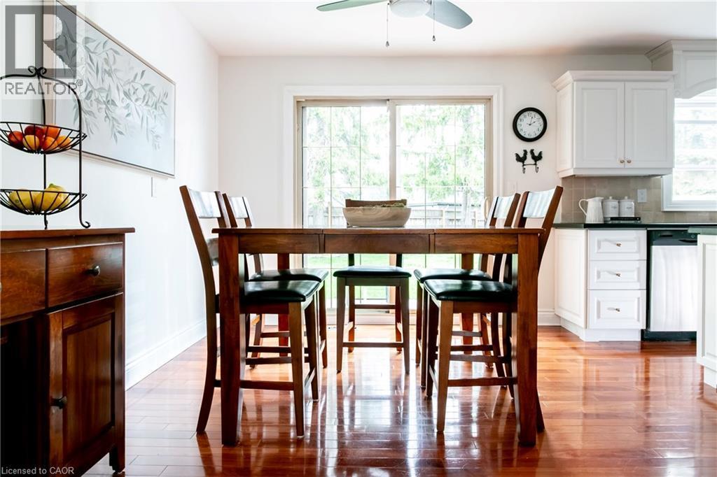 Open-concept dining area featuring wood-finish flooring, a sliding glass door, white baseboards, a ceiling fan, and white kitchen cabinetry with dark countertops - 1577 Old Spar Court, Mississauga, ON - Indoor Photo Showing Dining Room