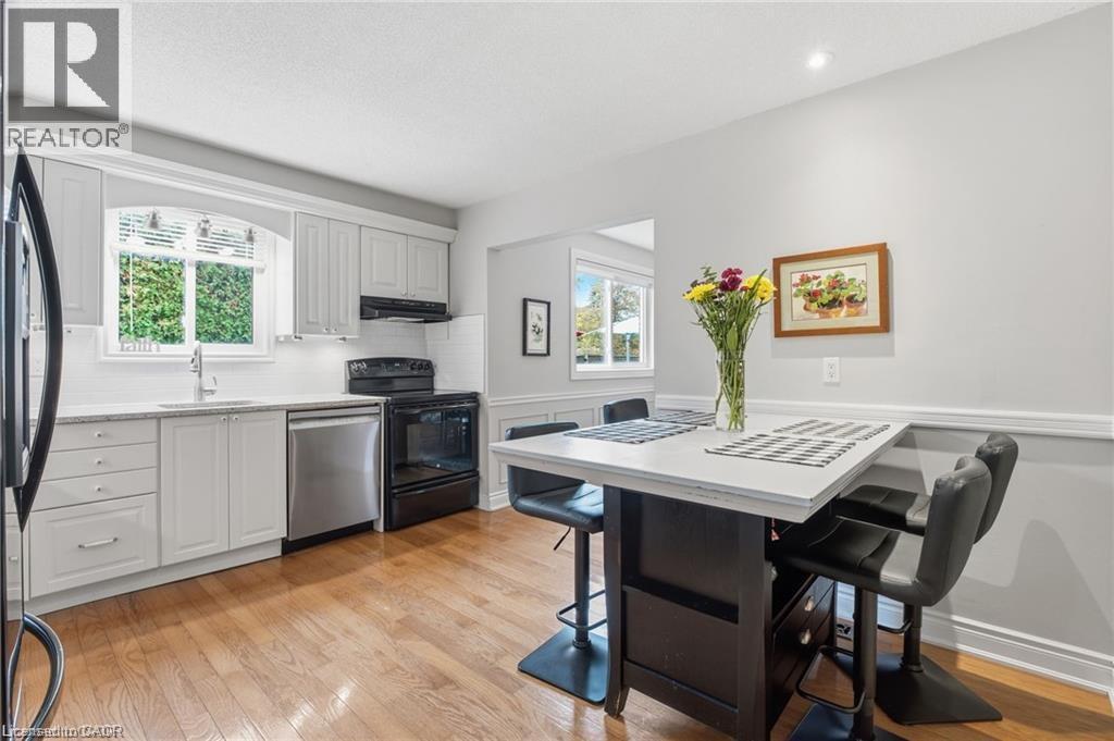 White eat-in kitchen with hardwood flooring and view to backyard - 668 Tomahawk Crescent, Ancaster, ON - Indoor Photo Showing Other Room