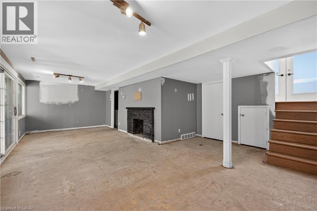 Spacious lower-level room featuring a dark stone fireplace, exposed wooden stairs with double doors, track lighting, and sliding glass doors - 515 Bobbybrook Drive, London, ON - Indoor Photo Showing Other Room