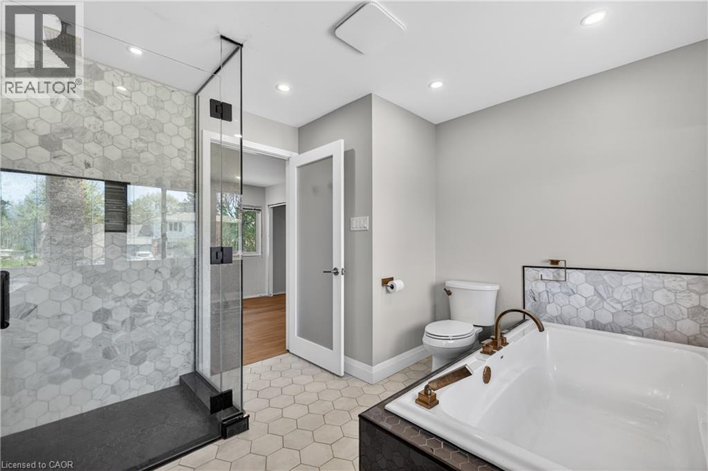 Bathroom featuring a frameless glass shower enclosure with hexagonal tile, a built-in soaking tub with bronze fixtures, hexagonal floor tiling, and recessed lighting - 515 Bobbybrook Drive, London, ON - Indoor Photo Showing Bathroom