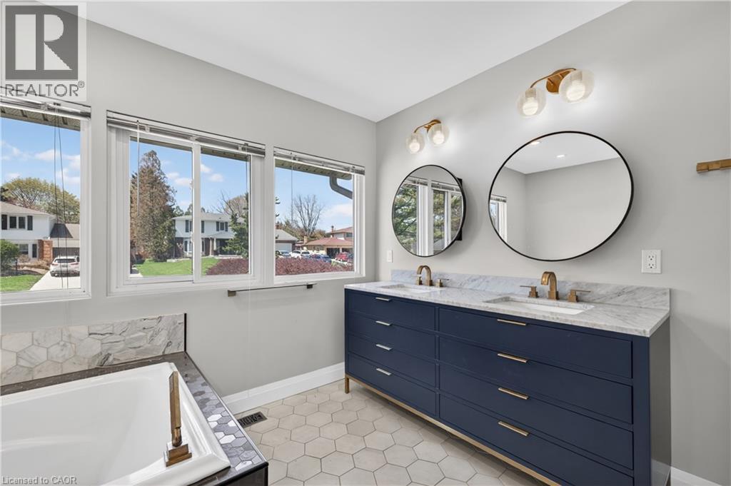 Bathroom featuring a double vanity with a blue cabinet and brass hardware, round mirrors, and dual wall-mounted light fixtures - 515 Bobbybrook Drive, London, ON - Indoor Photo Showing Bathroom