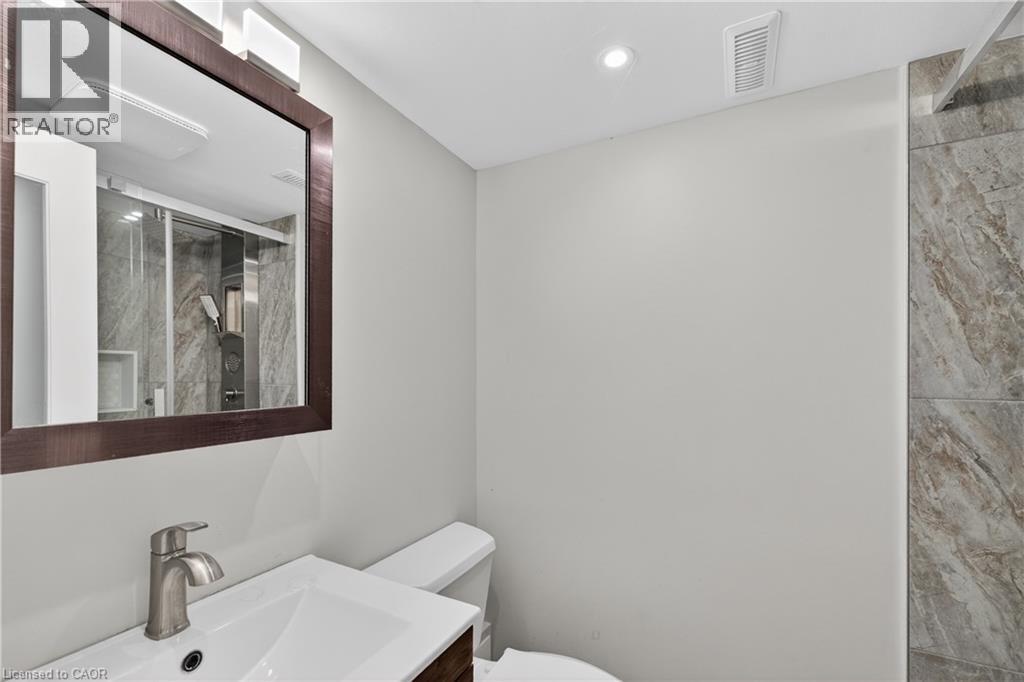 Bathroom featuring a framed mirror, vanity with an integrated sink and brushed nickel faucet, white toilet, and a tiled shower enclosure with a glass door - 515 Bobbybrook Drive, London, ON - Indoor Photo Showing Bathroom
