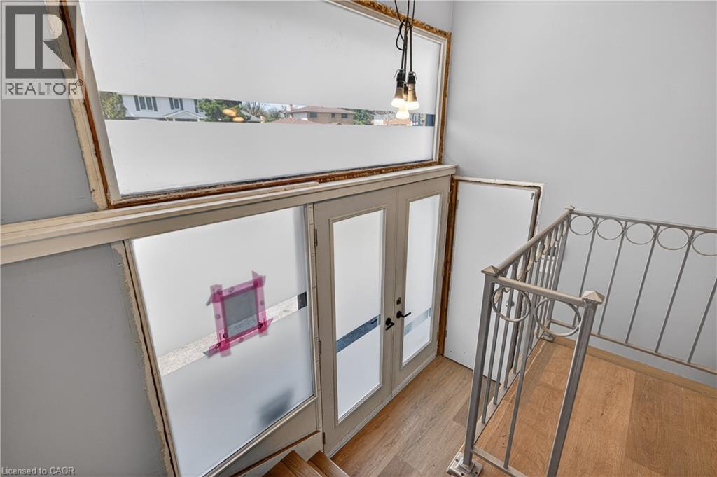 Stairwell featuring light wood-finish flooring, a decorative metal railing, a built-in pendant light fixture, and double glass-paneled doors with frosted lower sections - 515 Bobbybrook Drive, London, ON - Indoor Photo Showing Other Room