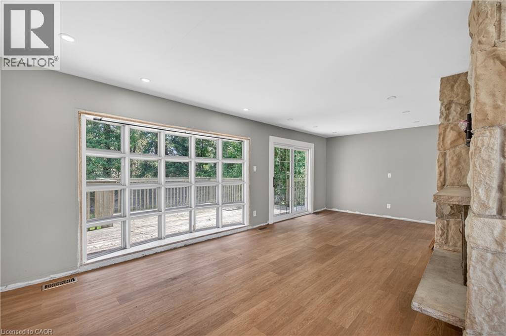 Spacious room featuring a large multi-pane window, wood-finish flooring, a stone-clad fireplace with a stone hearth, and recessed ceiling lighting - 515 Bobbybrook Drive, London, ON - Indoor