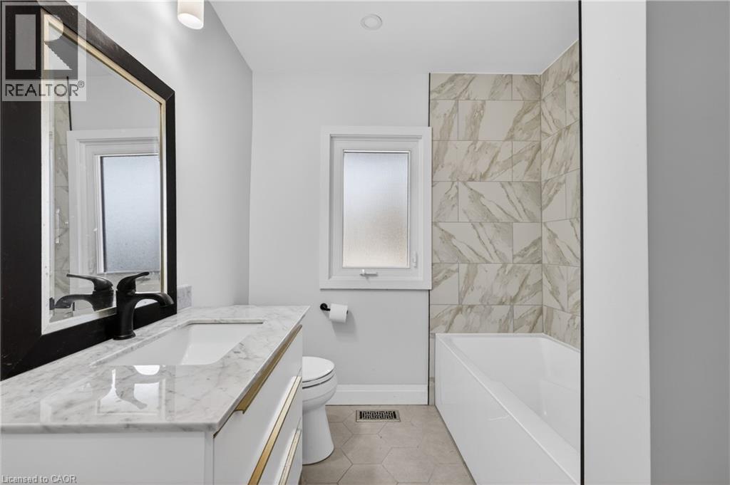 Contemporary bathroom featuring a white vanity with gold-tone hardware, a rectangular undermount sink, and a stone-finish countertop - 515 Bobbybrook Drive, London, ON - Indoor Photo Showing Bathroom