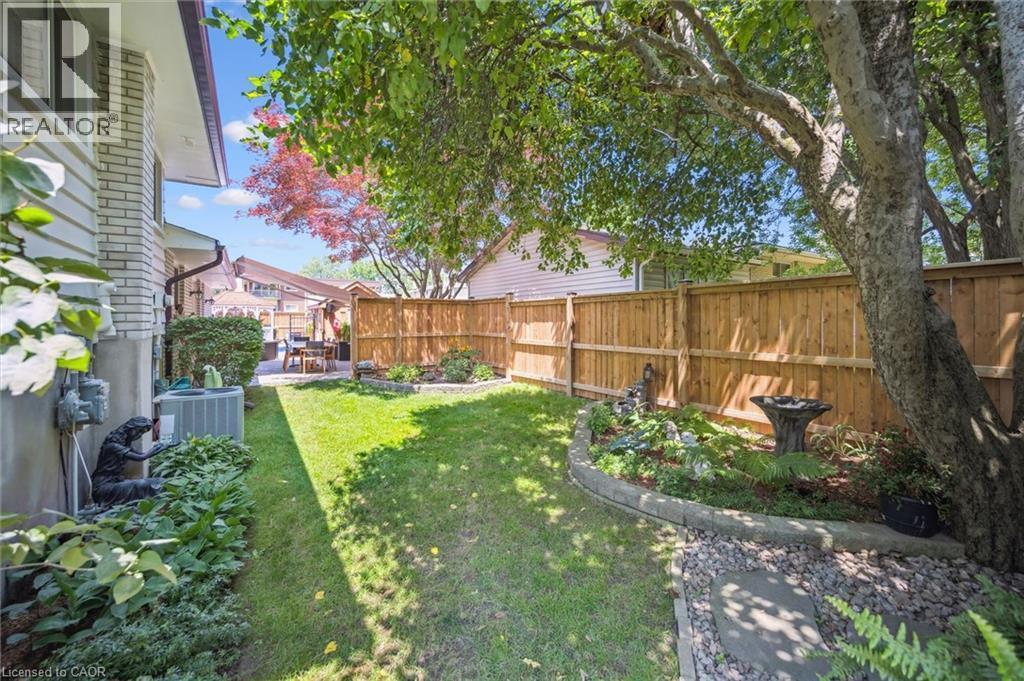Private backyard featuring a wooden privacy fence, mature trees, landscaped garden beds with stone borders, a stone pathway, and a patio area - 574 Sprucehill Avenue, Waterloo, ON - Outdoor