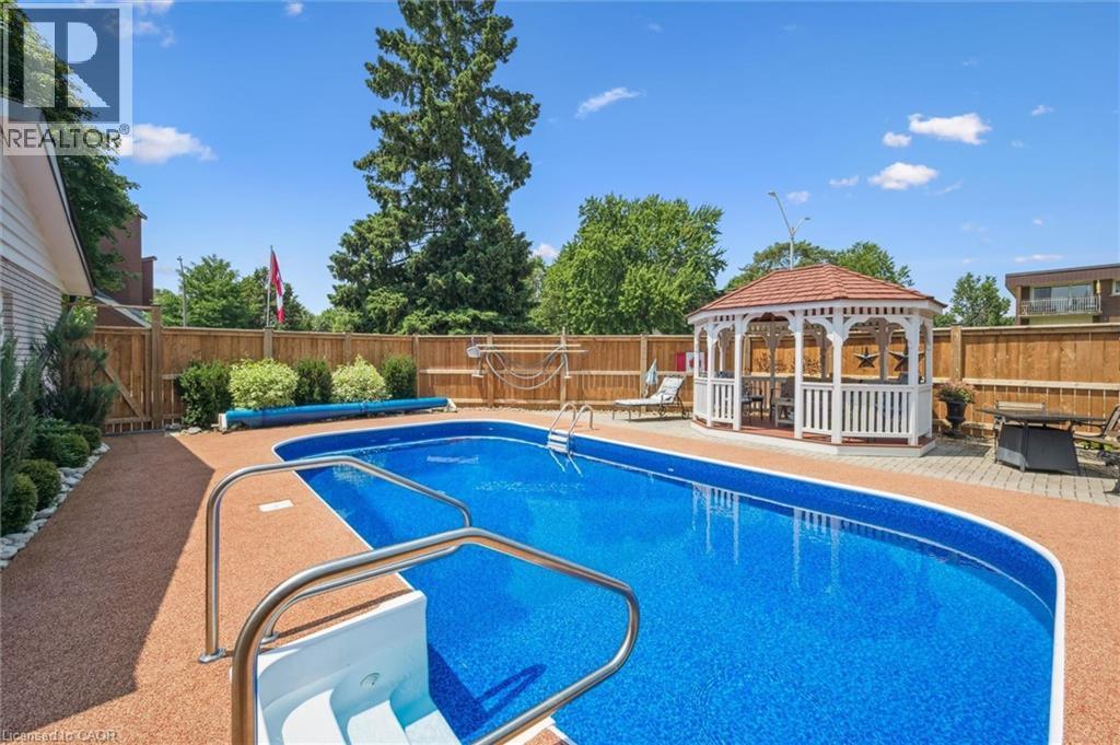 Backyard oasis featuring an in-ground swimming pool with integrated steps, a surrounding aggregate pool deck, and a white gazebo with a red shingle roof - 574 Sprucehill Avenue, Waterloo, ON - Outdoor With In Ground Pool With Deck Patio Veranda With Backyard