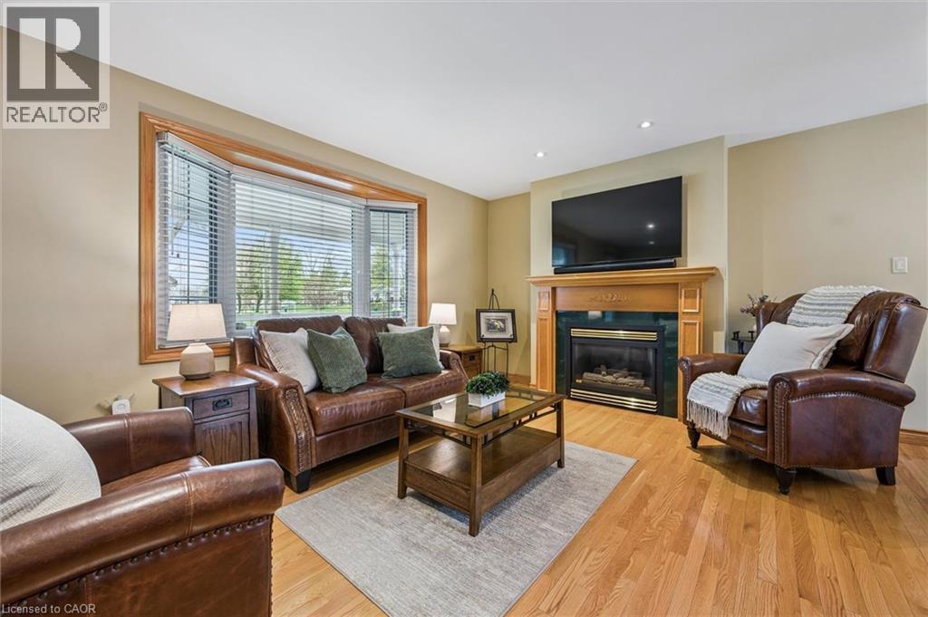 Living area featuring wood-finish flooring, a bay window with wood trim, recessed ceiling lighting, and a fireplace with a wood mantel and dark stone surround - 574 Sprucehill Avenue, Waterloo, ON - Indoor Photo Showing Living Room With Fireplace
