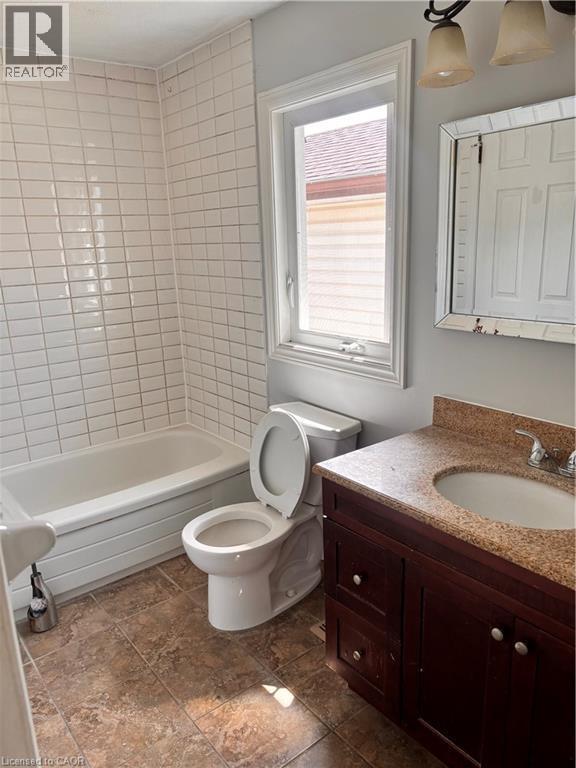 Bathroom featuring a white bathtub, subway tile surround, single-pane window, dark wood-finish vanity with an integrated sink, and a framed mirror - 206 Northmanor Crescent, Kitchener, ON