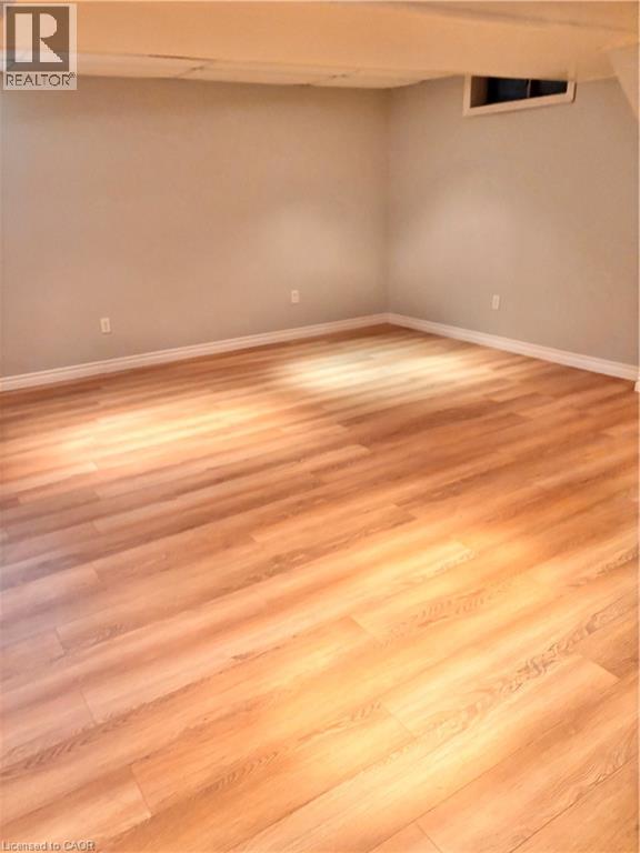 Spacious room featuring wood-finish flooring, light grey painted walls, white baseboards, and a window opening - 206 Northmanor Crescent, Kitchener, ON