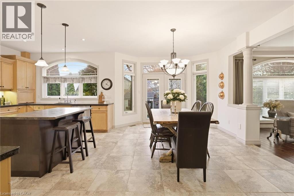 Spacious kitchen and dining area featuring stone tile flooring, light wood cabinetry, a dark kitchen island with countertop seating, and a bay window dining area with a multi-light chandelier - 129 Magnificent Way, Binbrook, ON - Indoor Photo Showing Dining Room