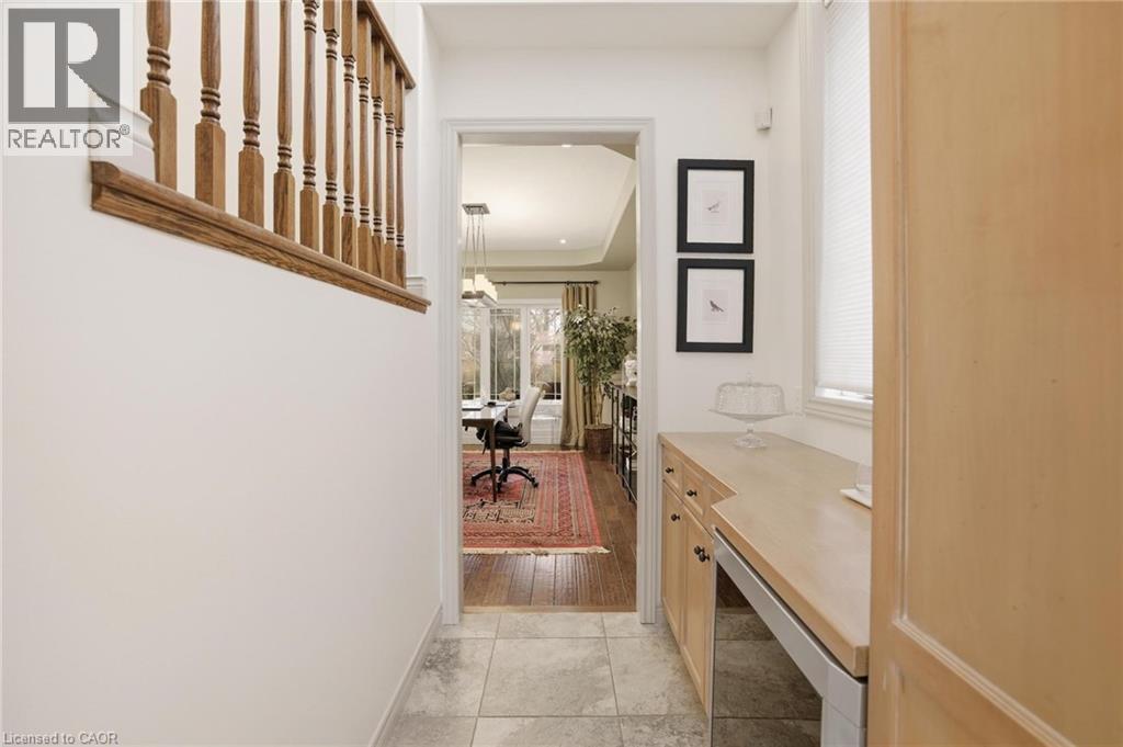 Hallway featuring tile flooring, a built-in desk area with light wood cabinetry, a window with blinds, and a wooden staircase railing - 129 Magnificent Way, Binbrook, ON - Indoor Photo Showing Other Room