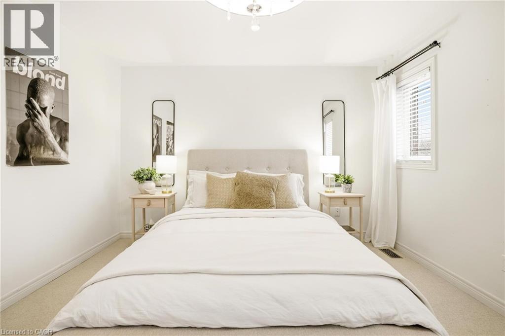 Carpeted bedroom featuring an upholstered headboard, white walls, and a window with blinds and white curtains - 129 Magnificent Way, Binbrook, ON - Indoor Photo Showing Bedroom
