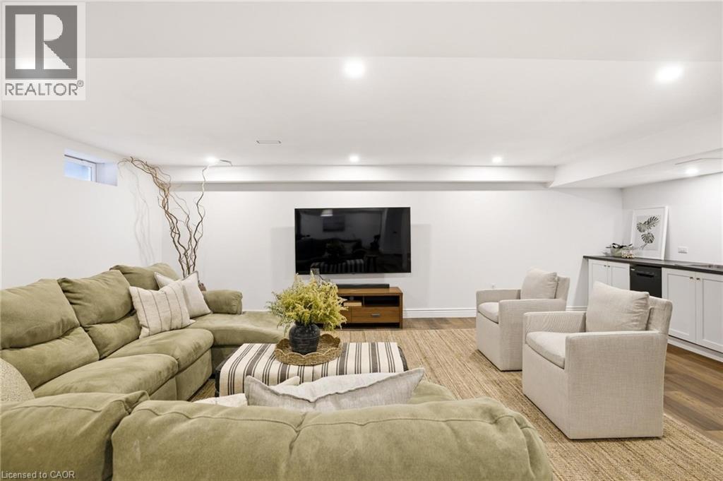 Spacious lower-level living area featuring recessed lighting, wood-finish flooring, a built-in wet bar with white cabinetry, and a window providing natural light - 129 Magnificent Way, Binbrook, ON - Indoor Photo Showing Living Room