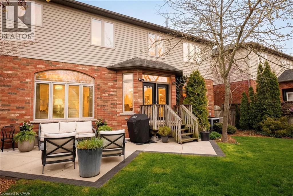 Rear exterior featuring a brick and siding facade, a ground-level concrete patio with contrasting border, a manicured lawn, an upper-level deck with wood railings, and mature trees and shrubs - 129 Magnificent Way, Binbrook, ON - Outdoor