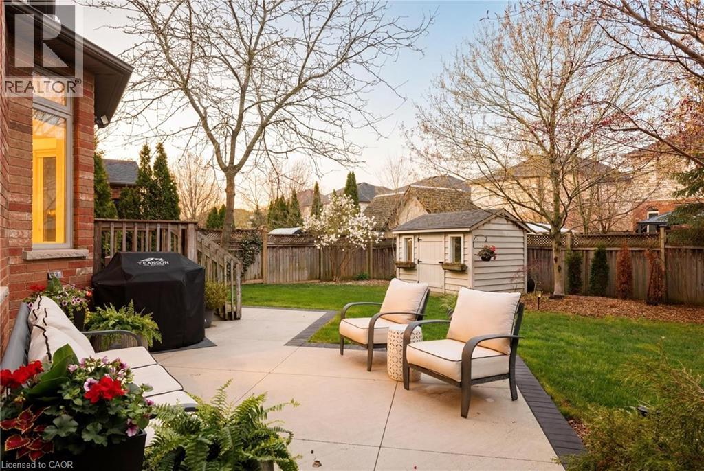 Expansive backyard featuring a large concrete patio, mature trees, a manicured lawn, and a wooden storage shed - 129 Magnificent Way, Binbrook, ON - Outdoor