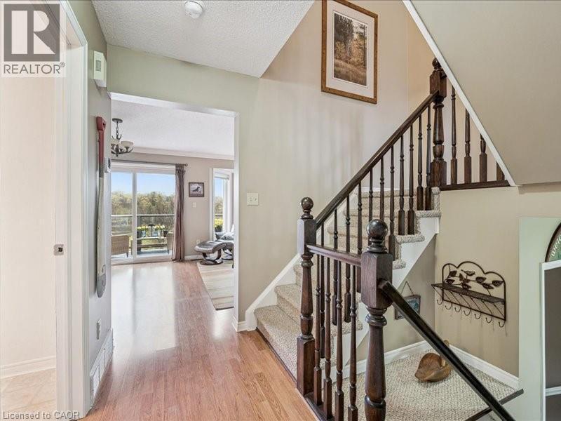 Entryway featuring wood-finish flooring, a carpeted staircase with dark wood banister, and an open doorway leading to a living area with a sliding glass door - 245 Bishop Street S Unit# 4, Cambridge, ON - Indoor Photo Showing Other Room
