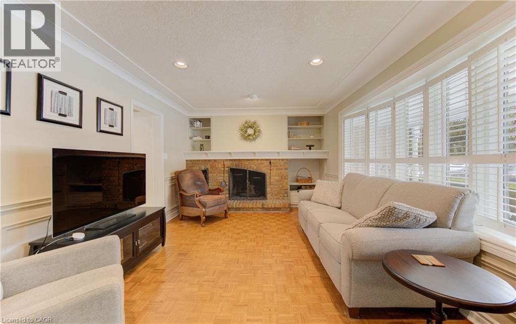 Living area featuring a brick fireplace with a white mantel, built-in shelving, wood-finish parquet flooring, recessed lighting, and large windows with plantation shutters - 514 Colonial Drive, Waterloo, ON - Indoor Photo Showing Living Room With Fireplace