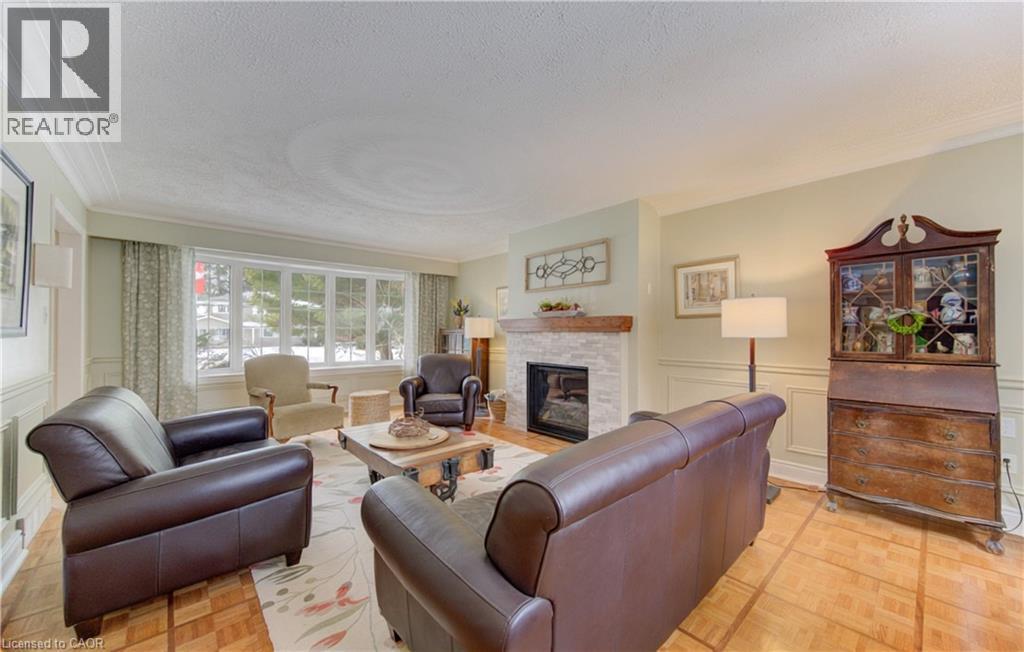 Living area featuring a stone-clad fireplace with a wood mantel, a multi-pane bay window, and wood-finish flooring - 514 Colonial Drive, Waterloo, ON - Indoor Photo Showing Living Room With Fireplace