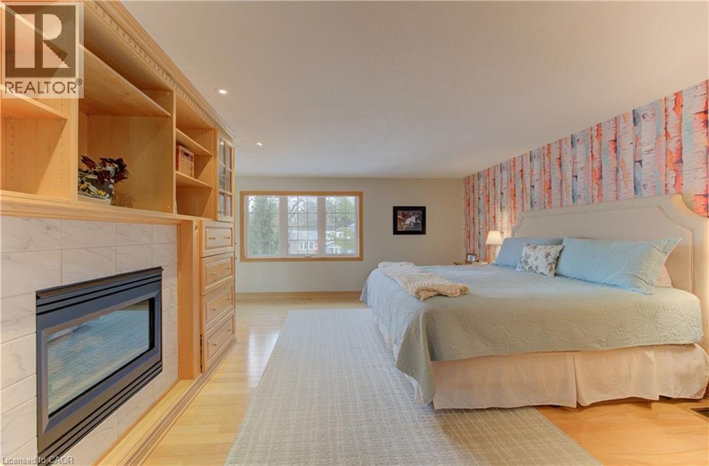 Light wood-finish flooring complements a built-in entertainment center featuring open shelving, glass-front cabinetry, and an integrated fireplace with a tiled surround - 514 Colonial Drive, Waterloo, ON - Indoor Photo Showing Bedroom With Fireplace