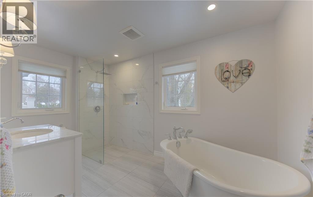 Contemporary bathroom featuring a freestanding soaking tub, a glass-enclosed shower with tiled walls and an integrated niche, a single vanity with a white countertop and undermount sink, and recessed - 514 Colonial Drive, Waterloo, ON - Indoor Photo Showing Bathroom