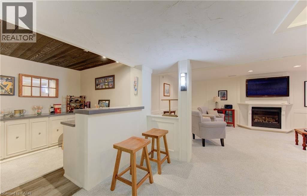 Finished lower level featuring a built-in wet bar with cabinetry, wood-finish flooring, a wall-mounted fireplace, and recessed lighting - 514 Colonial Drive, Waterloo, ON - Indoor Photo Showing Other Room With Fireplace