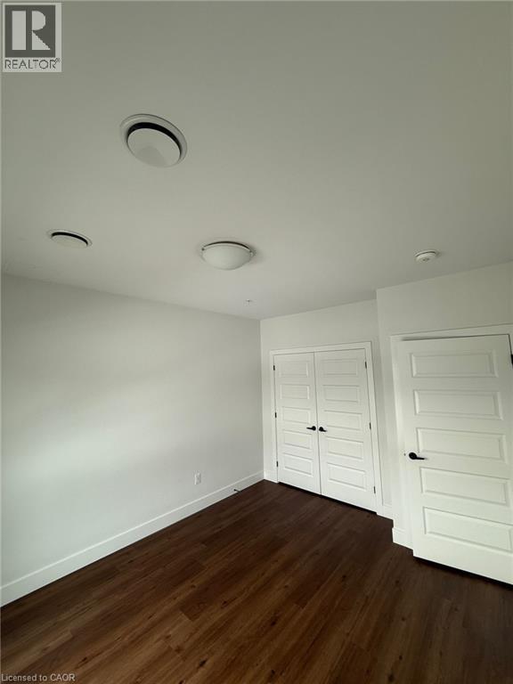 Unfurnished bedroom with a closet, dark wood-style floors, and baseboards - 1000 Lackner Place Unit# 401, Kitchener, ON - Indoor