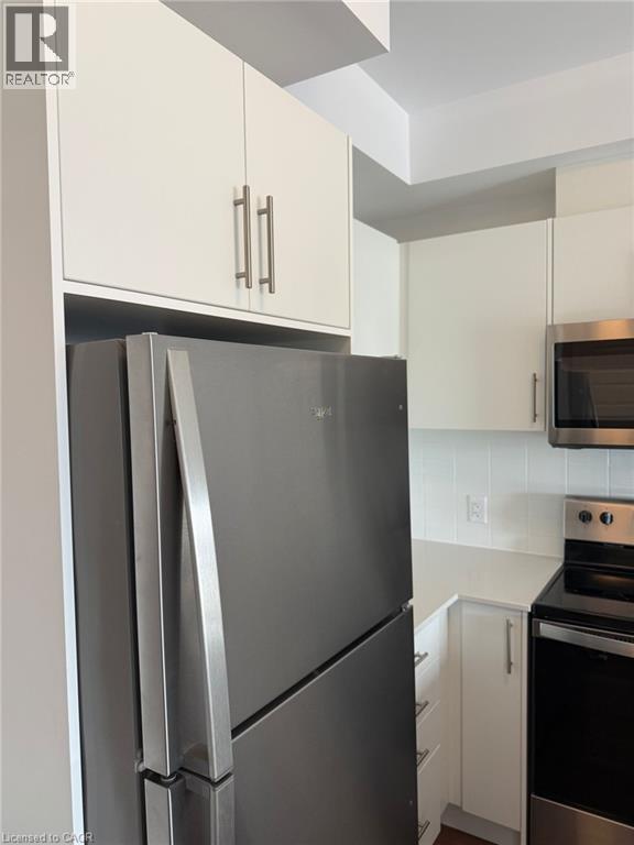 Kitchen with white cabinets, light countertops, backsplash, and stainless steel appliances - 1000 Lackner Place Unit# 401, Kitchener, ON - Indoor Photo Showing Kitchen