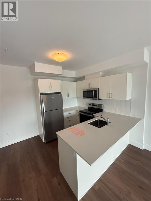Kitchen featuring light countertops, stainless steel appliances, dark wood finished floors, a sink, and a peninsula - 1000 Lackner Place Unit# 401, Kitchener, ON - Indoor Photo Showing Kitchen