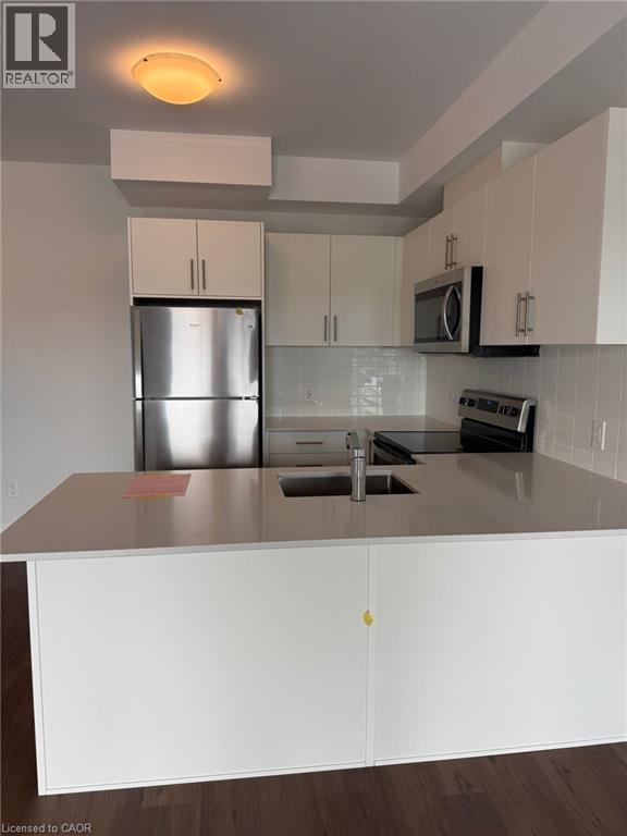 Kitchen featuring dark wood-style flooring, a peninsula, appliances with stainless steel finishes, a sink, and backsplash - 1000 Lackner Place Unit# 401, Kitchener, ON - Indoor Photo Showing Kitchen