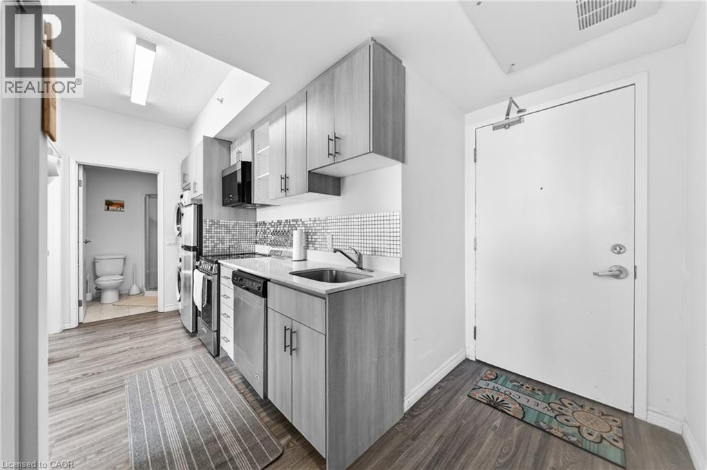 Compact kitchen featuring wood-finish flooring, light-toned cabinetry with dark hardware, stainless steel appliances, a mosaic tile backsplash, and a single basin sink - 246 Lester Street Unit# Ph-03, Waterloo, ON - Indoor Photo Showing Kitchen