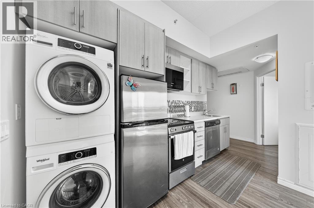 Compact kitchen featuring light wood-finish cabinetry, stainless steel appliances, a tile backsplash, and wood-finish flooring - 246 Lester Street Unit# Ph-03, Waterloo, ON - Indoor Photo Showing Laundry Room