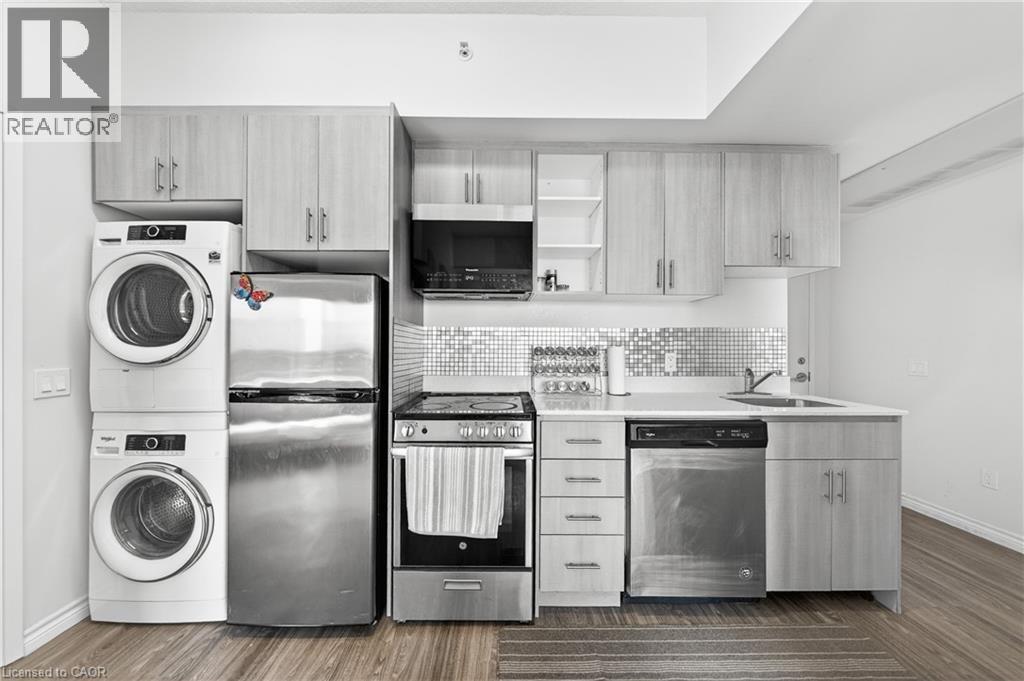 Compact kitchen featuring stainless steel appliances, stacked laundry units, light wood-finish cabinetry, a white countertop, and a mosaic tile backsplash - 246 Lester Street Unit# Ph-03, Waterloo, ON - Indoor Photo Showing Laundry Room