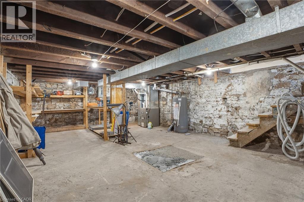 Unfinished basement featuring exposed wood ceiling joists, stone foundation walls, concrete flooring, and built-in wooden shelving - 137 Market Street, Hamilton, ON - Indoor Photo Showing Basement