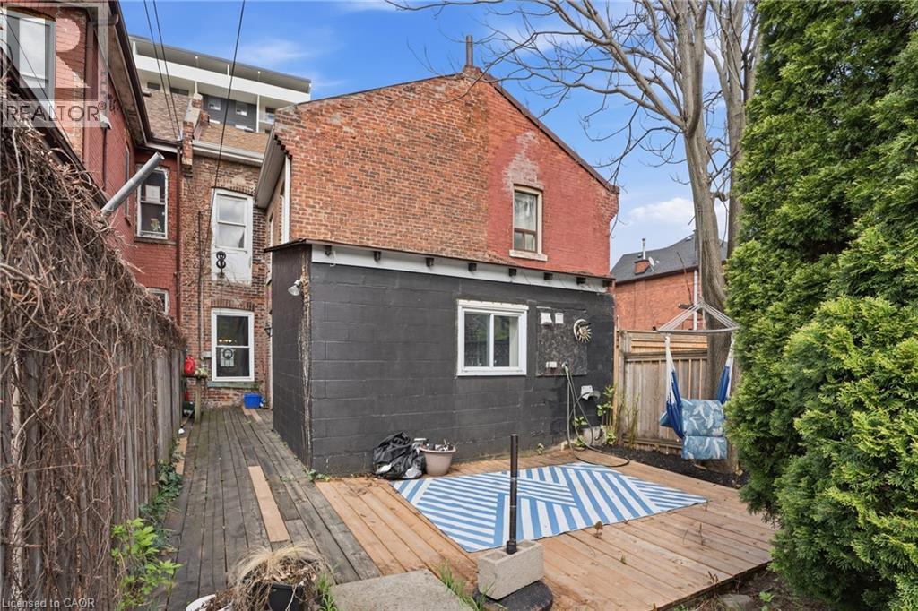 Rear exterior featuring a red brick facade with an attached black-painted extension, wood decking, and a privacy fence - 137 Market Street, Hamilton, ON - Outdoor With Exterior