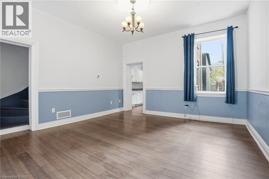 Spacious interior featuring wood-finish flooring, a decorative ceiling medallion with an attached chandelier, and a large window providing natural light - 137 Market Street, Hamilton, ON - Indoor Photo Showing Other Room