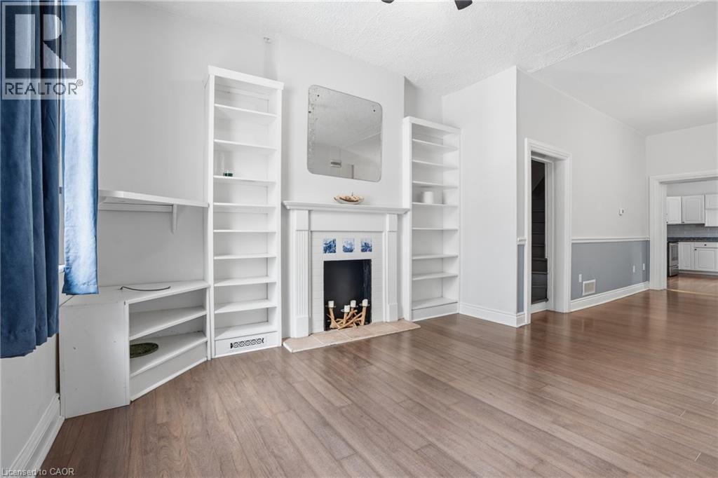 Spacious room featuring wood-finish flooring, a decorative fireplace with a mantel, built-in shelving, and white baseboards - 137 Market Street, Hamilton, ON - Indoor With Fireplace