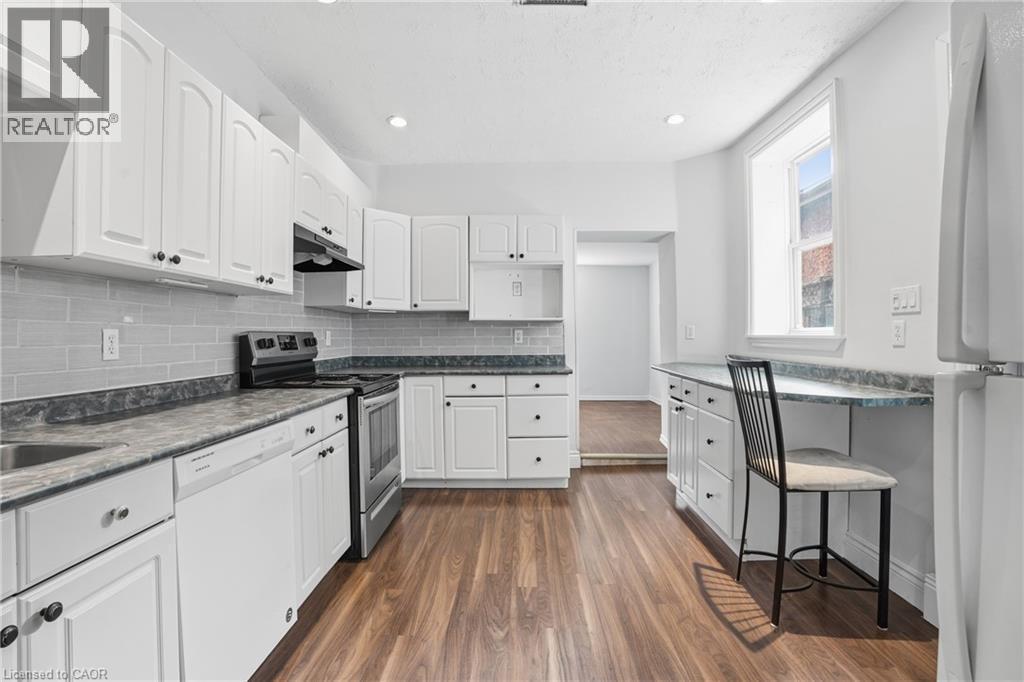 Bright kitchen featuring white cabinetry, grey subway tile backsplash, dark countertops, stainless steel appliances, and wood-finish flooring - 137 Market Street, Hamilton, ON - Indoor Photo Showing Kitchen