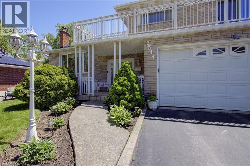 Stone veneer exterior with an integrated garage, upper-level balcony, and a paved driveway - 2344 Brinell Avenue, Burlington, ON - Outdoor With Balcony