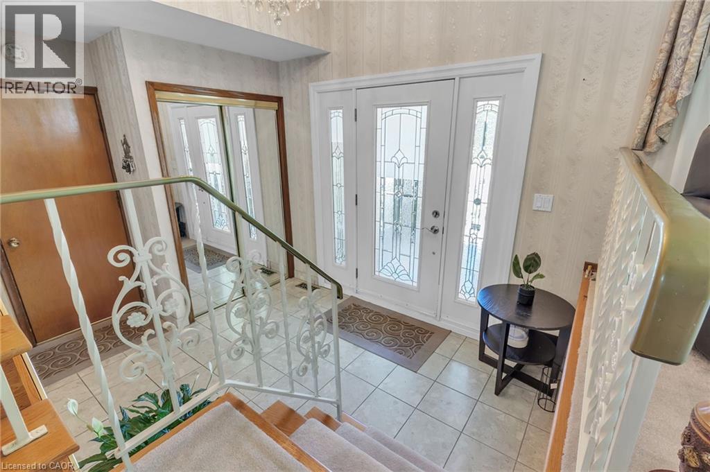 Entryway featuring a white double door with decorative glass inserts, ceramic tile flooring, and a wrought iron staircase railing - 2344 Brinell Avenue, Burlington, ON - Indoor Photo Showing Other Room